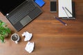 Laptop with office supplies, crumpled paper, green plant and hot black coffee with smoke on vintage grunge wooden desk background Royalty Free Stock Photo