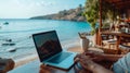 Laptop open on a beachfront table, blending work and leisure with a beautiful coastal backdrop.