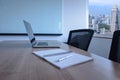 Laptop and pen on notepad for agenda kept on table in empty corporate conference room with cityscape view on background.