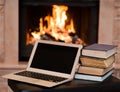 Laptop and pile of books against the background of the fireplace