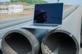 Laptop on pipes at a construction site. Reflection of a portrait of a builder in a helmet on the screen.