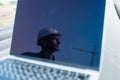 Laptop on pipes at a construction site. Reflection of a portrait of a builder in a helmet on the screen.