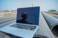 Laptop on pipes at a construction site. Reflection of a portrait of a builder in a helmet on the screen.