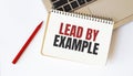 Laptop, red pen and notepad with text LEAD BY EXAMPLE in the white background Royalty Free Stock Photo