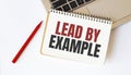 Laptop, red pen and notepad with text LEAD BY EXAMPLE in the white background Royalty Free Stock Photo