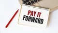 Laptop, red pen and notepad with text PAY IT FORWARD in the white background Royalty Free Stock Photo