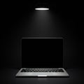 A laptop with a sleek, closed design is centered under a lone overhead lamp, casting Royalty Free Stock Photo