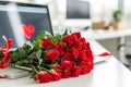 laptop standing at workplace in office,on monitor of which heart is painted,and next to it lies bouquet of scarlet roses,concept