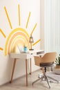 Laptop, stationery and lamp on table near wall with painted sun indoors. Interior design Royalty Free Stock Photo