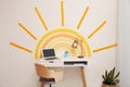 Laptop, stationery and lamp on table near wall with painted sun indoors. Interior design Royalty Free Stock Photo