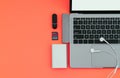 Laptop with USB Type-C adapter, flash drives, headphones and Power Bank on a red background, top view, workplace