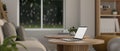 A laptop on a wooden coffee table in a cozy minimalist living room. rear view