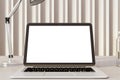Laptop on a wooden desk with lamp and striped curtain, focused work environment.