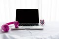 The laptop working near alarm clock and pink headphone listen music on the white bed in the sunny day morning holiday. Royalty Free Stock Photo