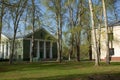 A large abandoned building of light yellow color in the Empire style stands on a green meadow. tall deciduous trees grow around