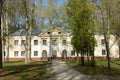 A large abandoned building of light yellow color in the Empire style stands on a green meadow. tall deciduous trees grow around