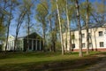 A large abandoned building of light yellow color in the Empire style stands on a green meadow. tall deciduous trees grow around