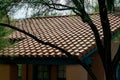 Large adobe style roof tiles with slanted double gable architecture in late evening shade and sun with front yard tree