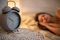 A large alarm clock stands on the cabinet next to the sleeping young woman. Royalty Free Stock Photo