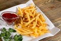 Large amounts of golden fries on a curly square plate with ketchup and parsley