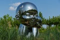 Large baby heads with smiling faces in mirrored metal. Sculpture installation Inner Child by sculptor Ken Kellehe