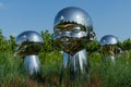 Large baby heads with smiling faces in mirrored metal. Sculpture installation Inner Child by sculptor Ken Kellehe in city park