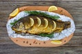 Large baked carp with herbs, lemon and spices in foil on a wooden background.