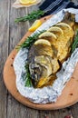 Large baked carp with herbs, lemon and spices in foil on a wooden background.