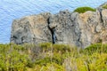 Large Bare Rocks with Scars and a Hole. Detailed Stone Wall with Grass and Bushes. Blue Sea in Background in Crete Island, Greece Royalty Free Stock Photo