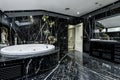 large bathroom tiled with black marble with black veins, circular whirlpool bathtub and black furniture with mirror embedded in Royalty Free Stock Photo