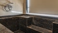 The large bathtub is lined with black marble tiles.