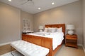 A large bedroom with light wood furniture and a bench at the end of the bed.