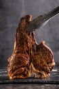 Large beef roast T-bone steak with smoke. Head chef holding steak meat tongs on a black background. copy space