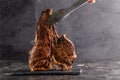 Large beef roast T-bone steak with smoke. Head chef holding steak meat tongs on a black background. copy space