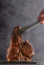 Large beef roast T-bone steak with smoke. Head chef holding steak meat tongs on a black background. photon image copy space