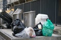 Large black bags of garbage lie on the sidewalk in the city next to the steel trash cans