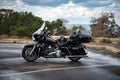 Large black custom motorcycle parked at a lookout with clouds in the background