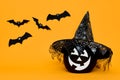 Large Black Halloween Pumpkin with cute smiling face wearing witch hat looking at flying bats over orange background. Royalty Free Stock Photo