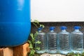 A large blue barrel and 4 smaller plastic bottles filled with water on the facade of a house