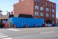 A large blue dumpster on a street near a large brick building with orange reflective warning barrels Royalty Free Stock Photo