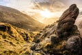 Large boulder and valley with water reservoir, dramatic sunset with sunrays. Mourne Mountains