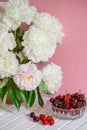 A large bouquet of peonies in a ceramic vase on the table, cherries in a bowl. Royalty Free Stock Photo