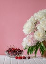A large bouquet of peonies in a ceramic vase on the table, cherries in a bowl Royalty Free Stock Photo
