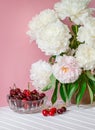 A large bouquet of peonies in a ceramic vase on the table, cherries in a bowl Royalty Free Stock Photo