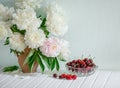 A large bouquet of peonies in a ceramic vase on the table, cherries in a bowl. Royalty Free Stock Photo