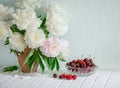 A large bouquet of peonies in a ceramic vase on the table, cherries in a bowl Royalty Free Stock Photo