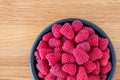 Large bowl of fresh red raspberries for dessert, black ceramic bowl, light wood background Royalty Free Stock Photo