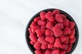 Large bowl of fresh red raspberries for dessert, black ceramic bowl, white marble background Royalty Free Stock Photo