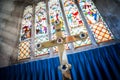 Large brass gold cross with sparkling jewels stood in the sun at front of Church of England chapel with big tall colourful stained