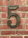 Large brass number five mounted on a red brick wall